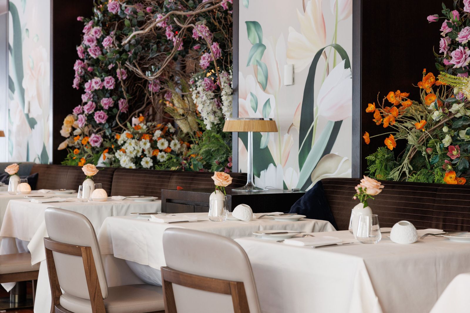 White-linen dining room with peach roses, floral murals, and lush blossom displays along the wall