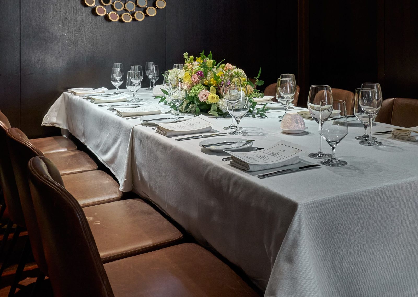 Private dining table set with white linens, crystal glassware, menus and a pastel floral centerpiece
