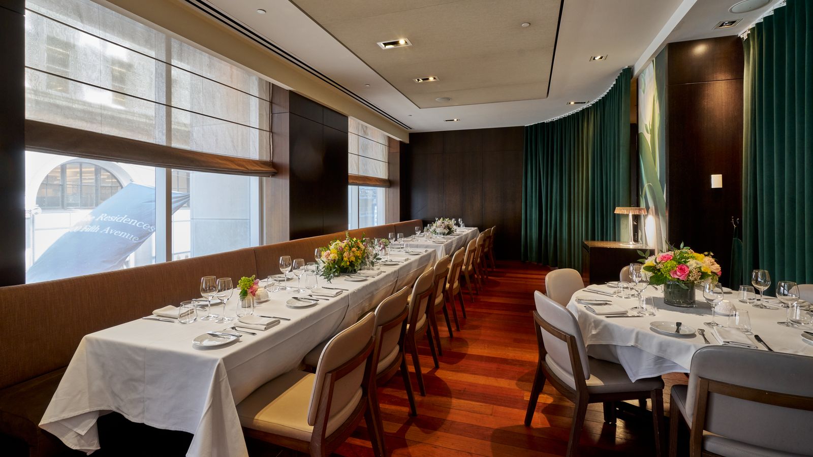 Private dining room with a long white-linen banquette table, floral centerpieces and green drapes
