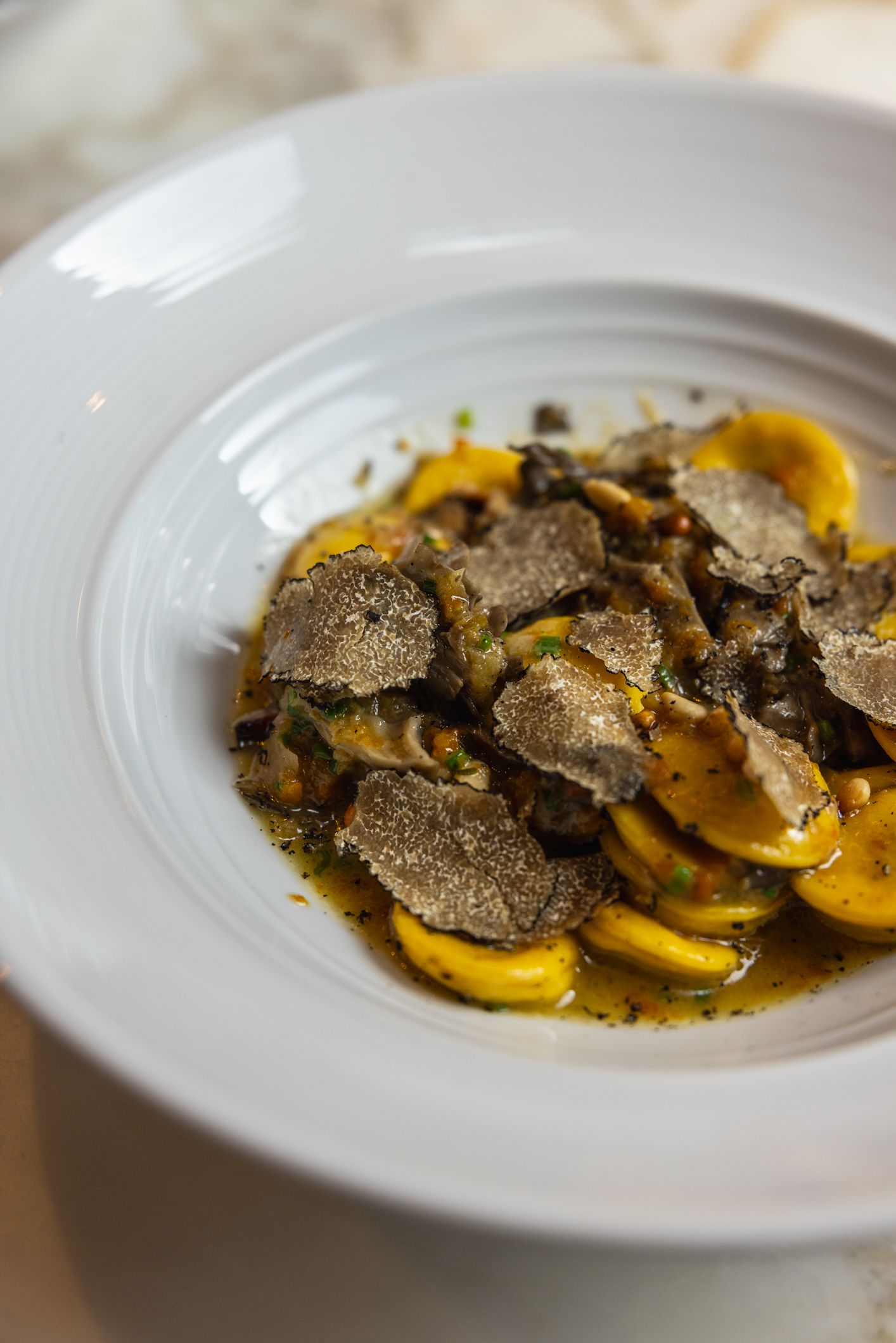 Golden agnolotti in brown butter broth crowned with shaved black truffle and mushrooms