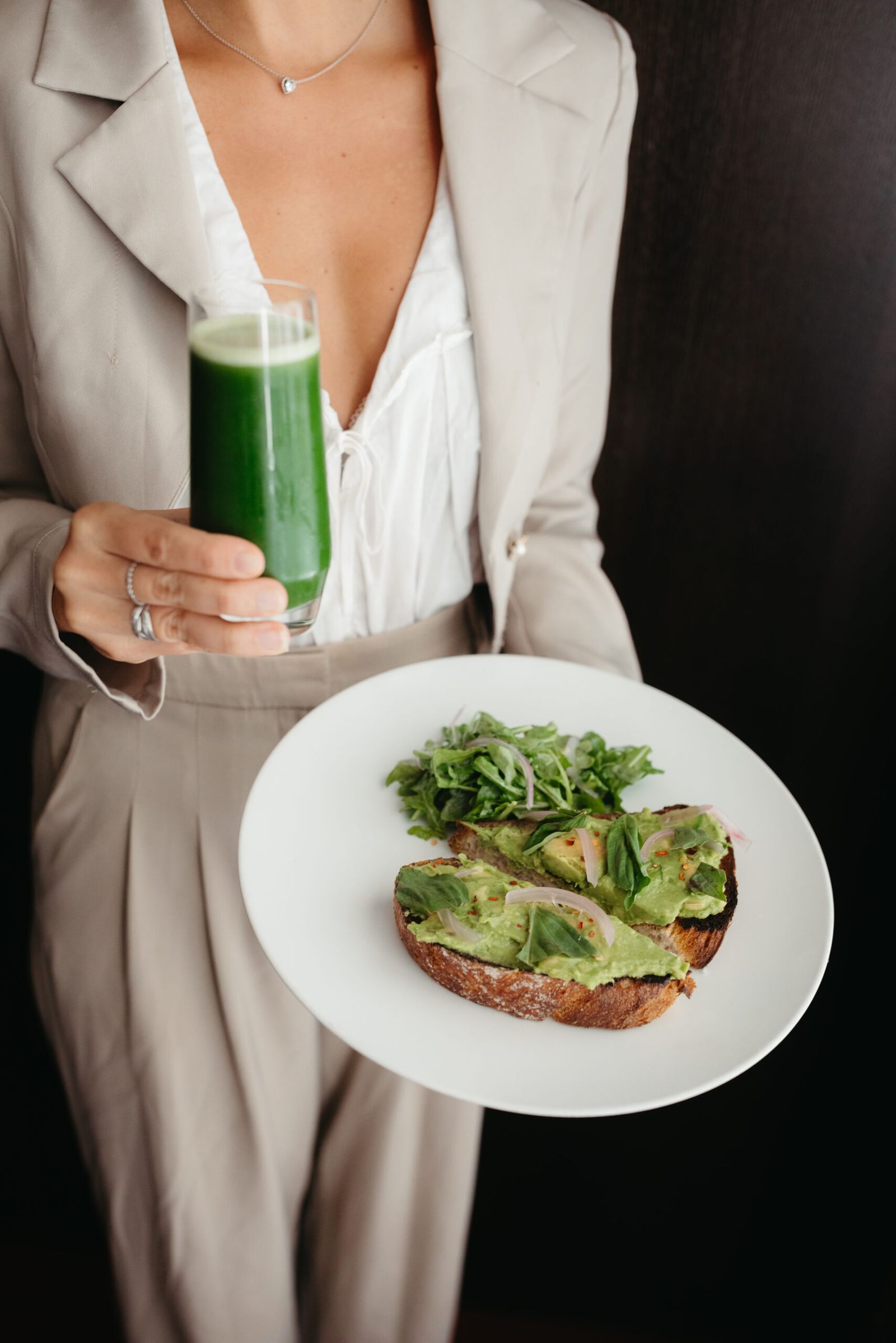 a woman holding a glass of green juice and a plate of avocado toast