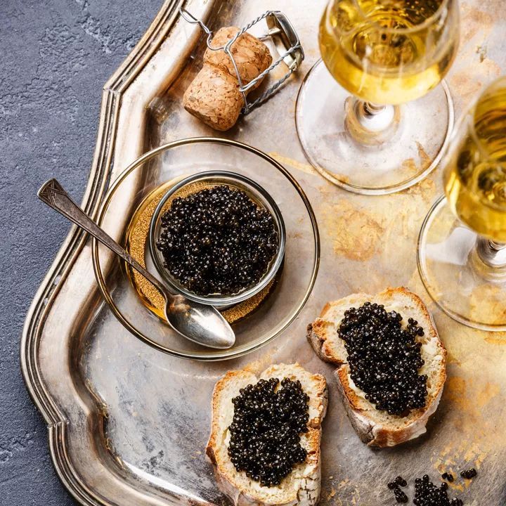 Black caviar in a glass jar with toast points and sparkling wine on a silver tray