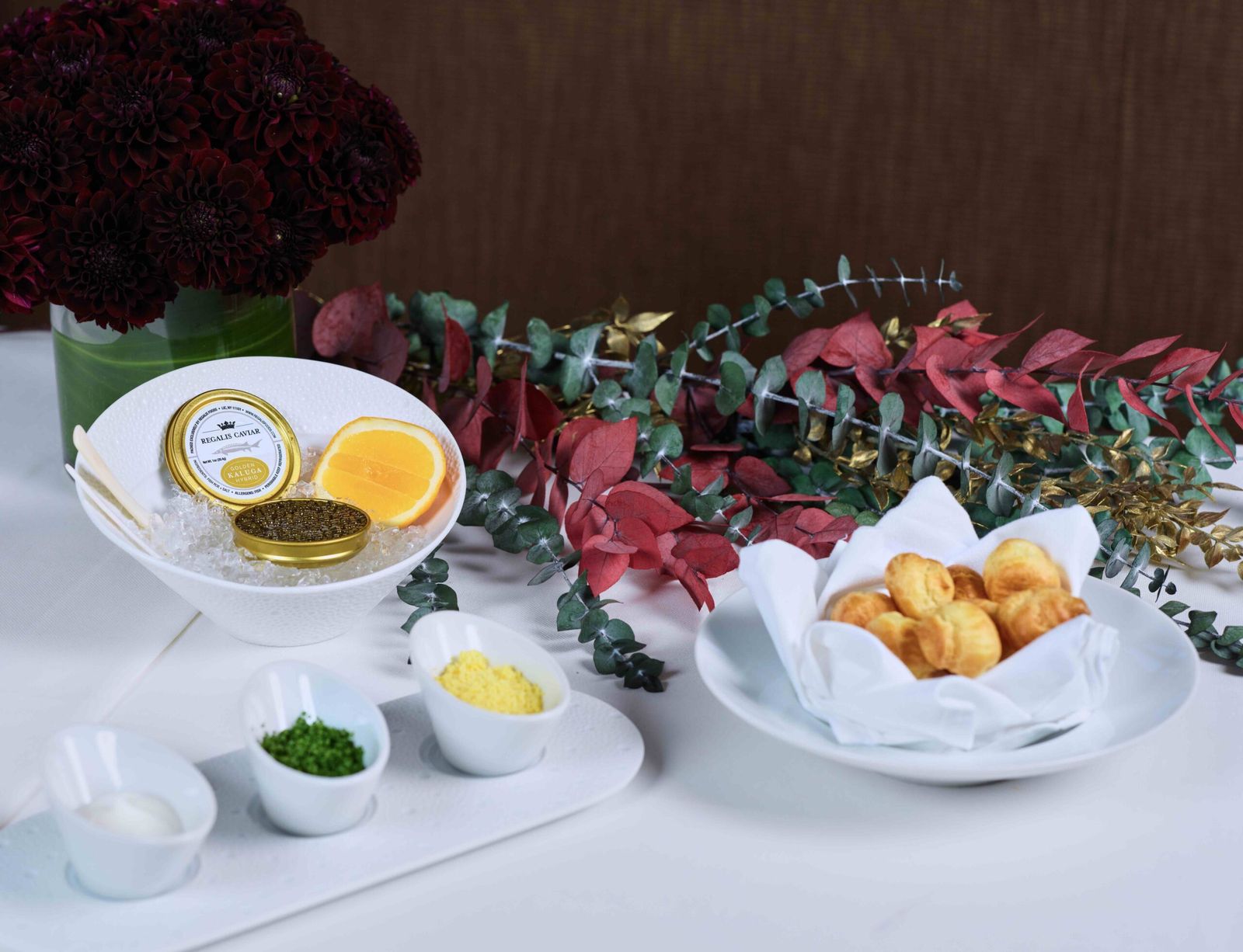 Golden Kaluga caviar on ice with orange, chive and egg garnishes beside warm gougères