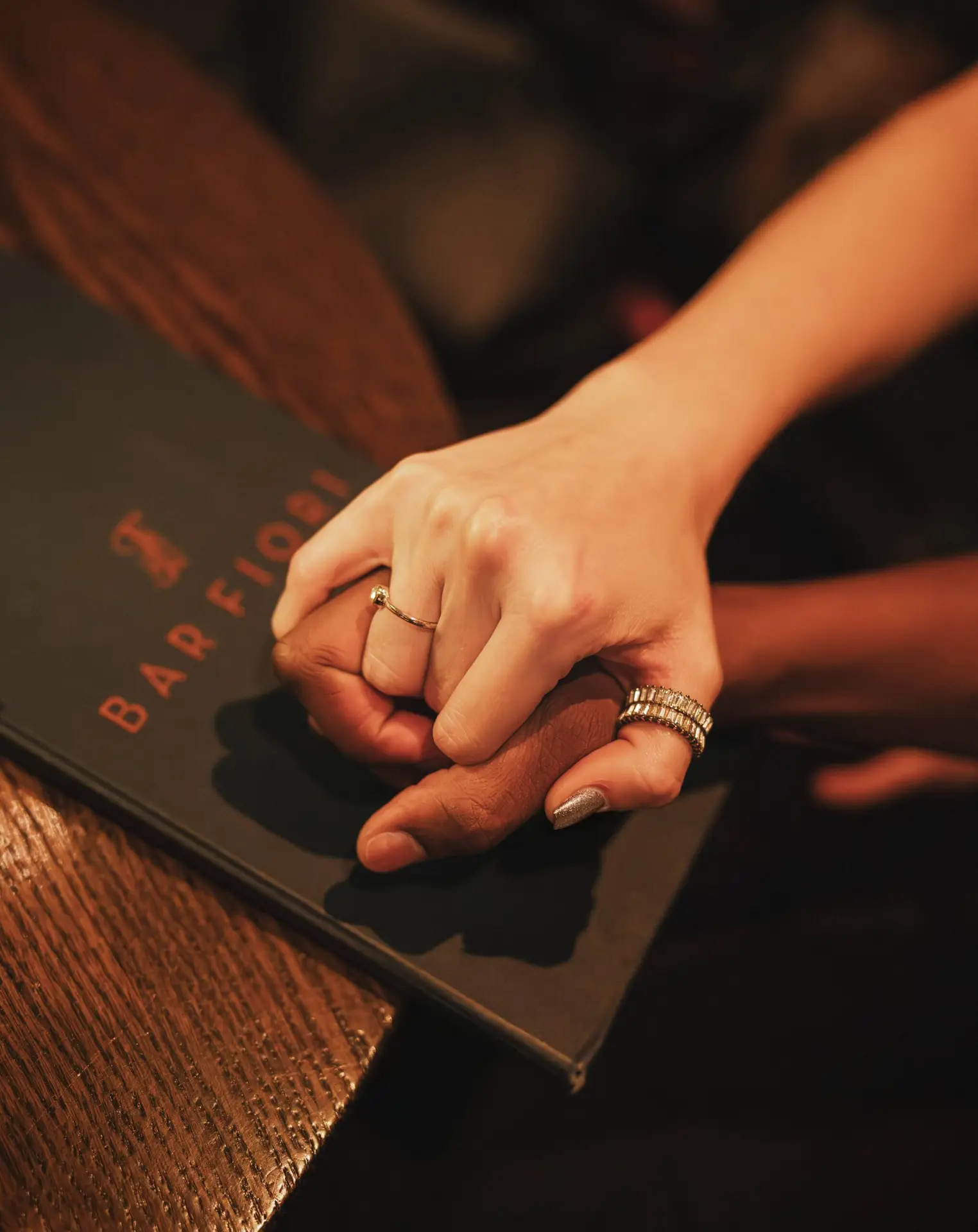 lose-up of two people holding hands on a restaurant table next to a bar menu