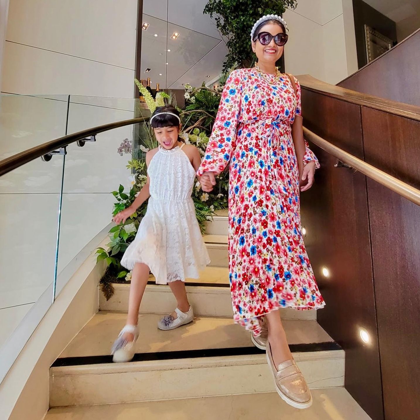 Woman in floral midi dress and young girl in white dress descending a marble staircase