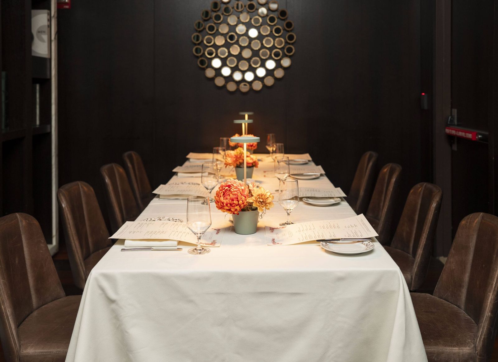 Elegant private dining room with long table set for dinner, floral centerpieces, and leather chairs