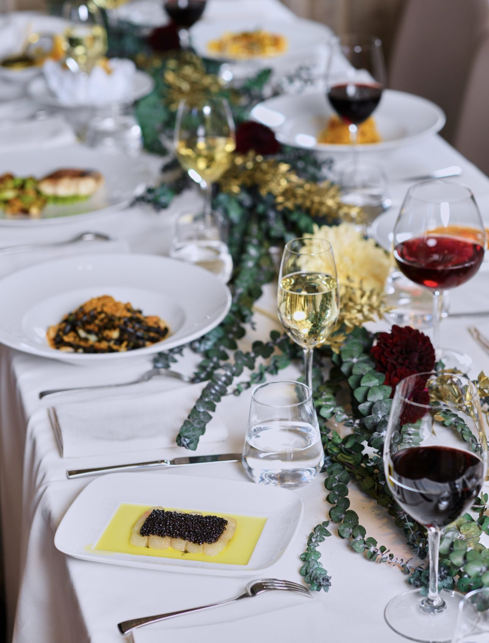 Elegant holiday table set with caviar, pasta courses, wine glasses and eucalyptus garland