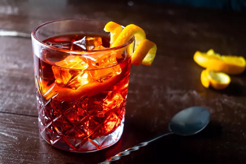 Negroni over ice in a cut-crystal glass with orange peel on a dark wood table