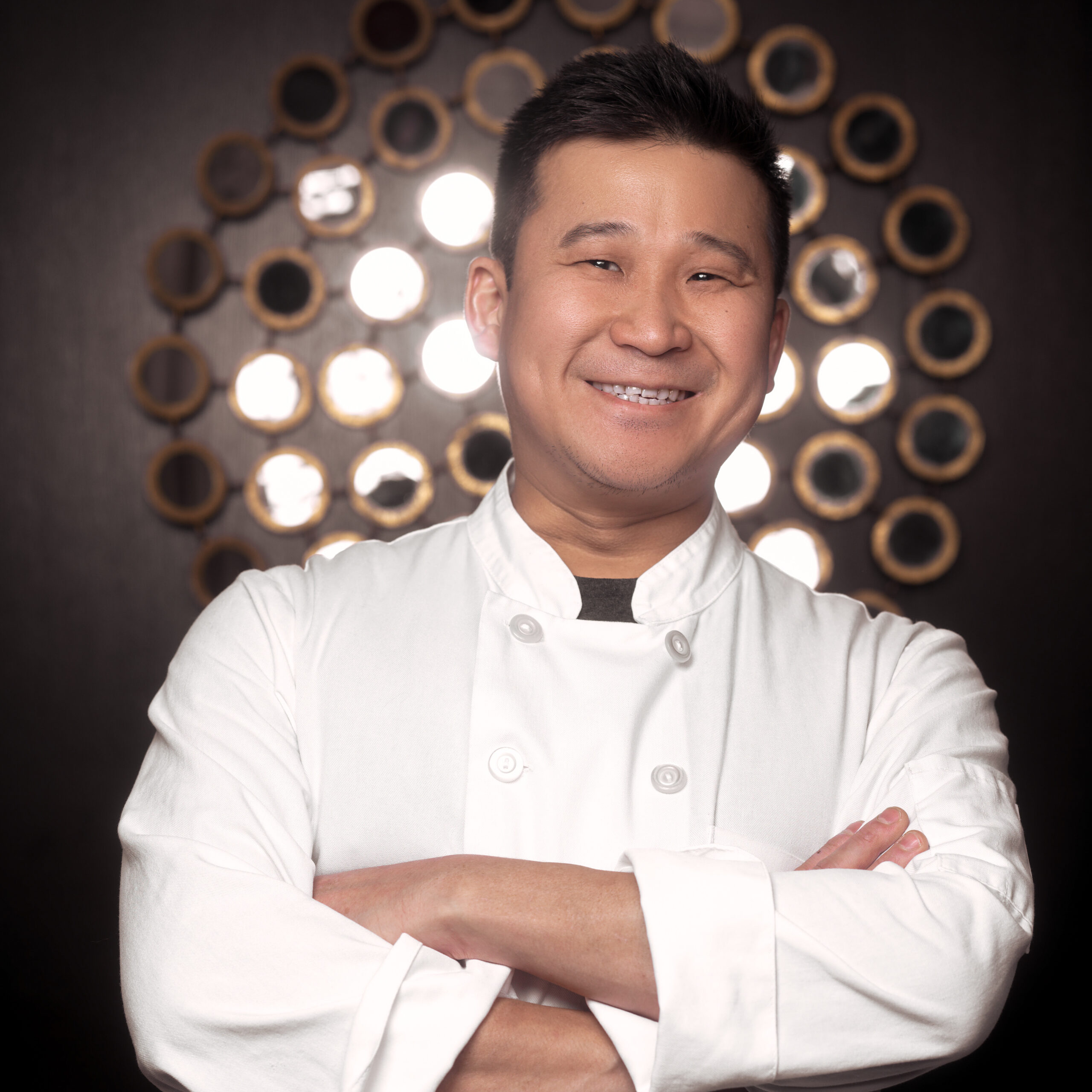 a smiling man in a white chef's coat with crossed arms