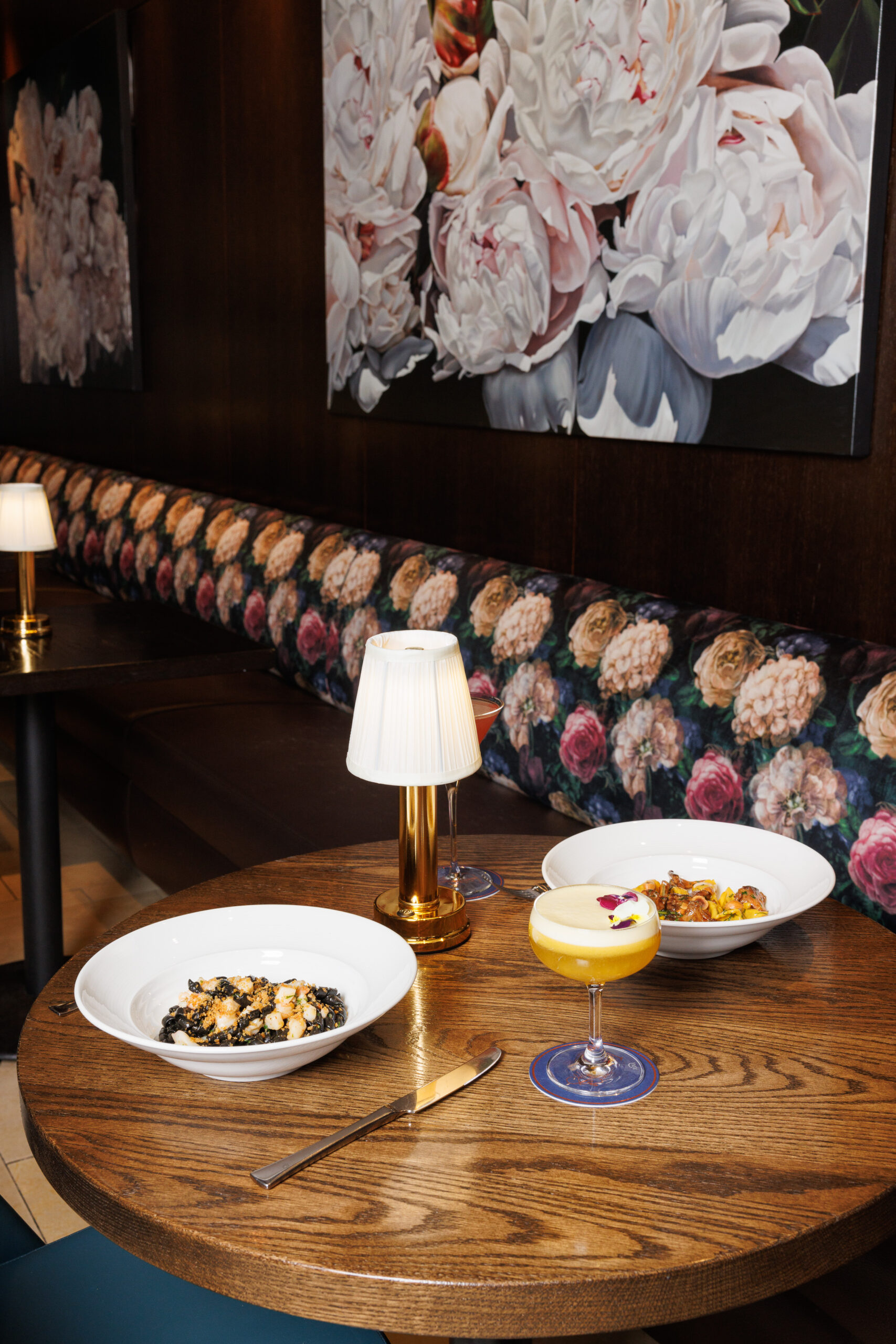 bar fiori, decorated with floral paintings and a floral patterned banquet, and two dishes of pastas along with a cocktail on their wooden table