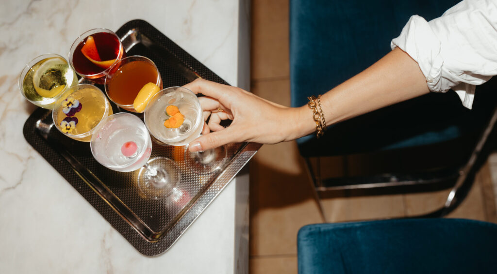 a hand selects from a group of different cocktails on a tray