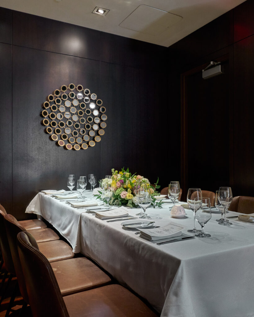 ai fiori's semi-private imperia table, a long white tablecloth-covered table surrounded by two dark wood walls and lined with brown leather chairs