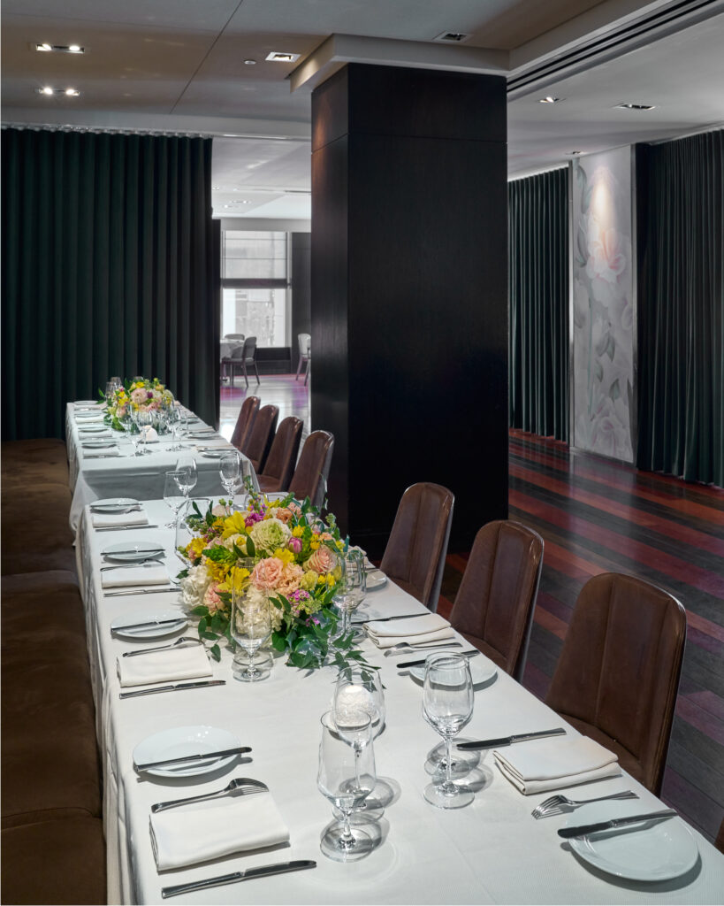 ai fiori's semi-private savona table for events - a long table with a white tablecloth, set with white napkins and plates. vibrant floral arrangements are placed along the center